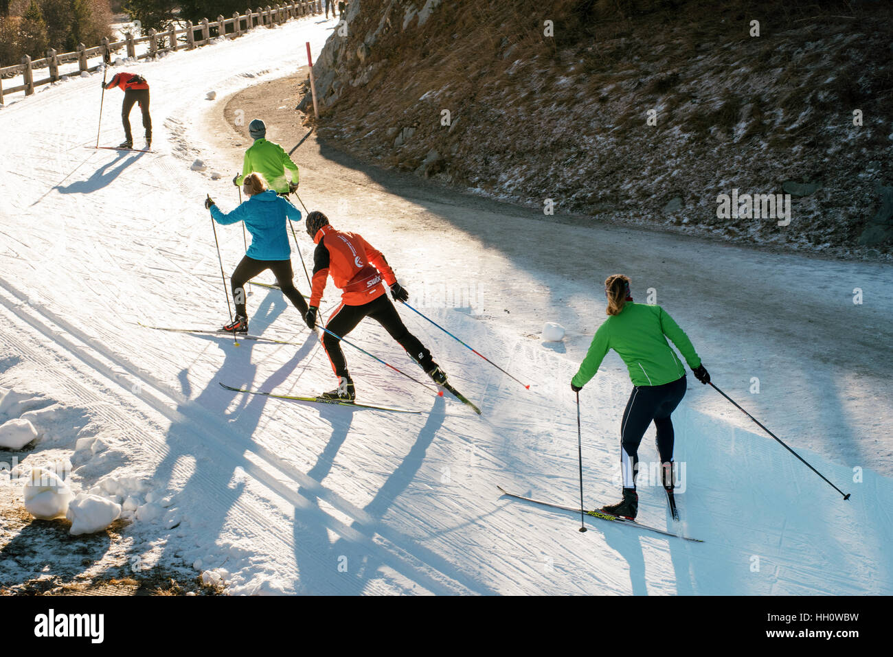 Team of young people cross country skiing training on a winding mountain road in colorful ski clothes Stock Photo