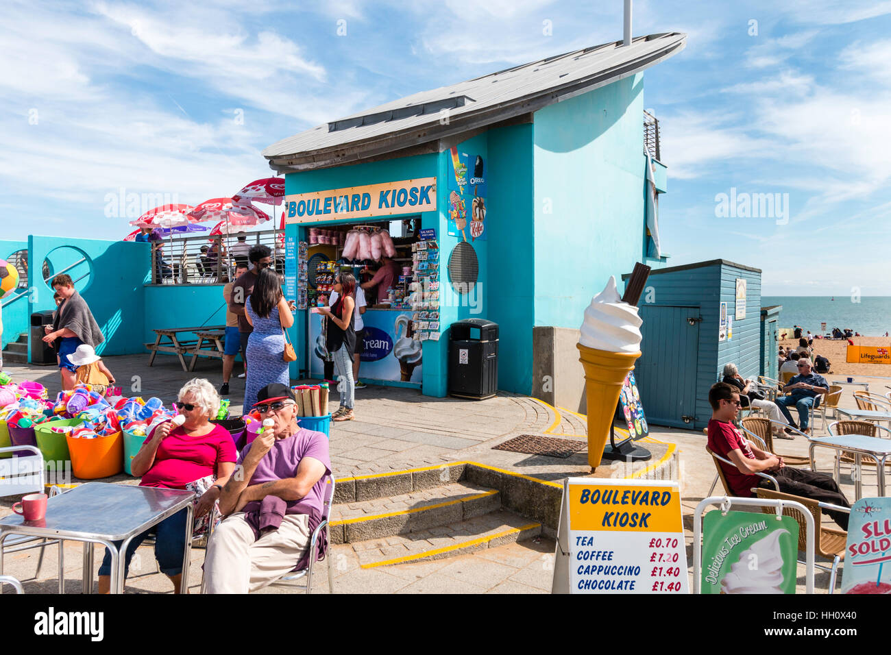 England, Ramsgate. People sitting with ice creams outside small blue kiosk on seafront in bright sunshine during summer heatwave Stock Photo