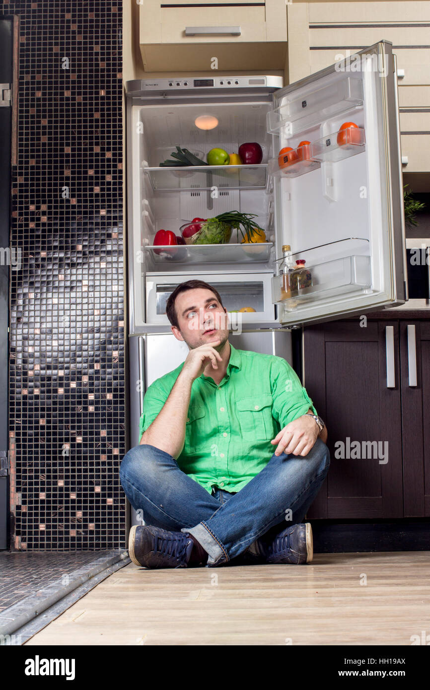 Young Man Sitting on the floor In Front Of Fridge with fruits and