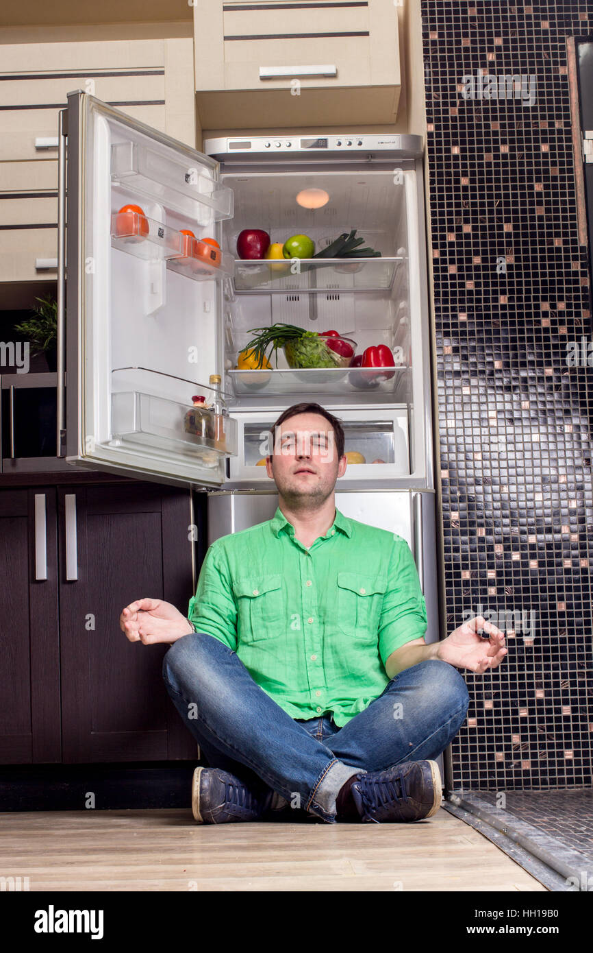 Young Man Sitting on the floor In Front Of Fridge with fruits and