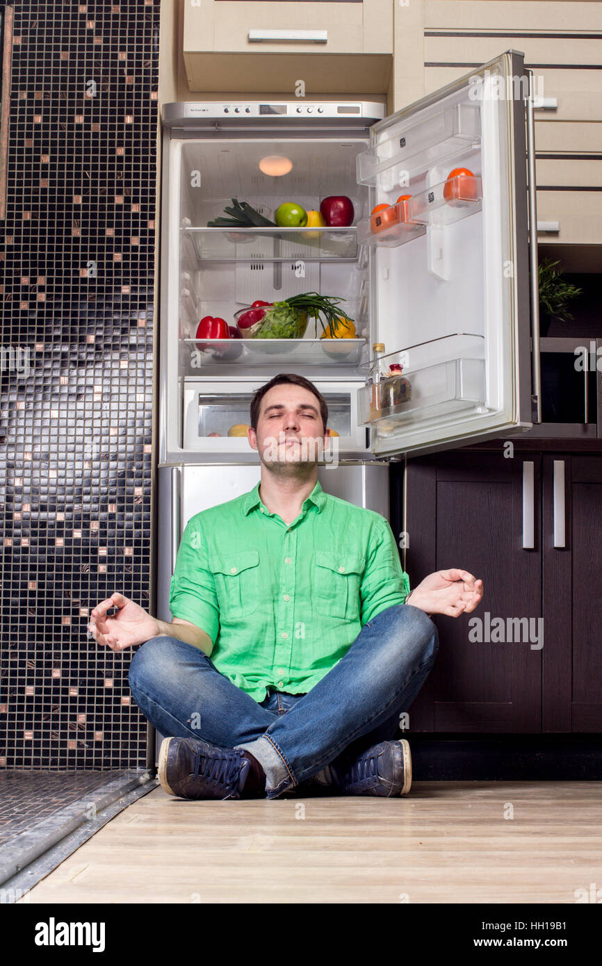 Young Man Sitting on the floor In Front Of Fridge with fruits and