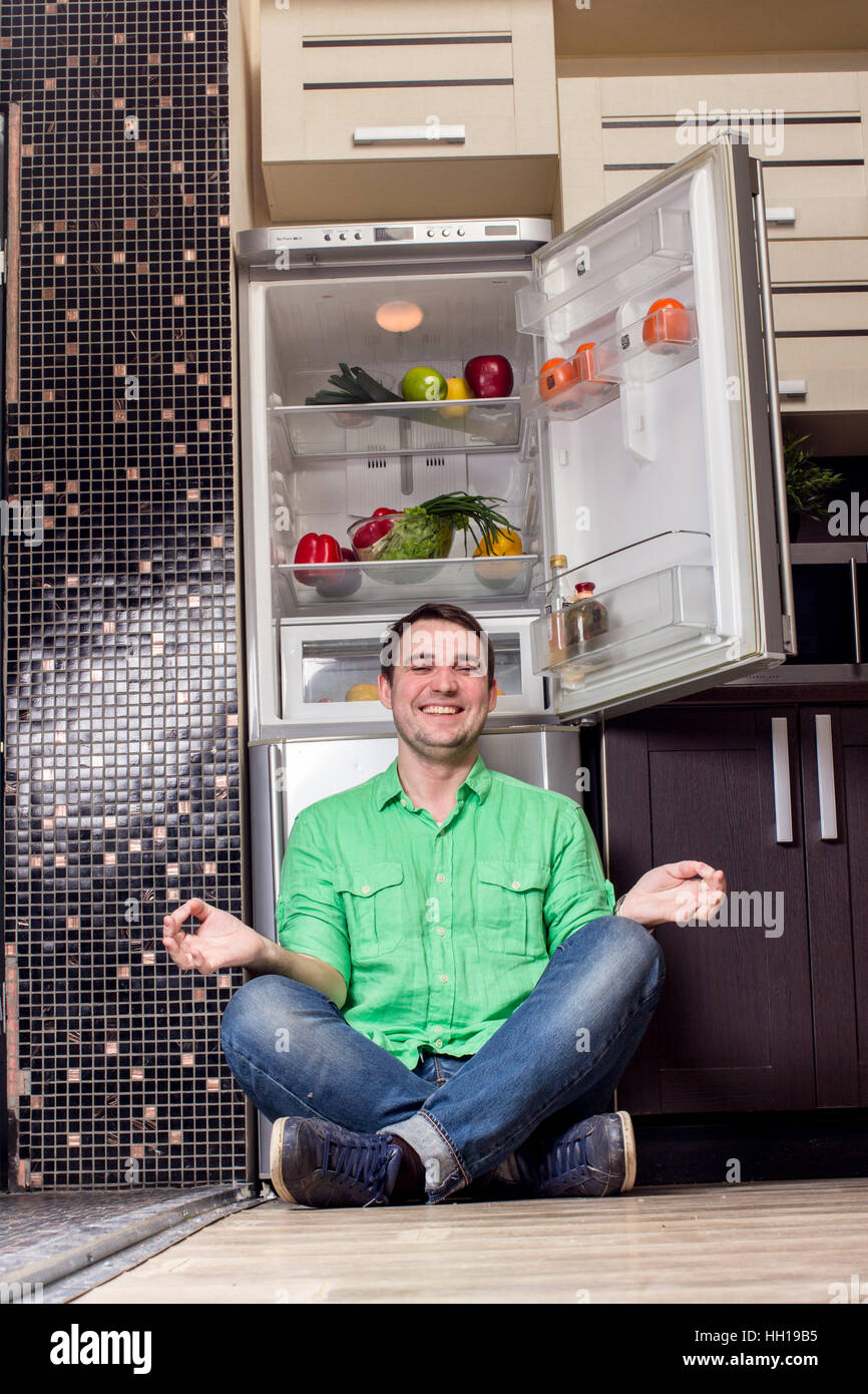 Young Man Sitting on the floor In Front Of Fridge with fruits and