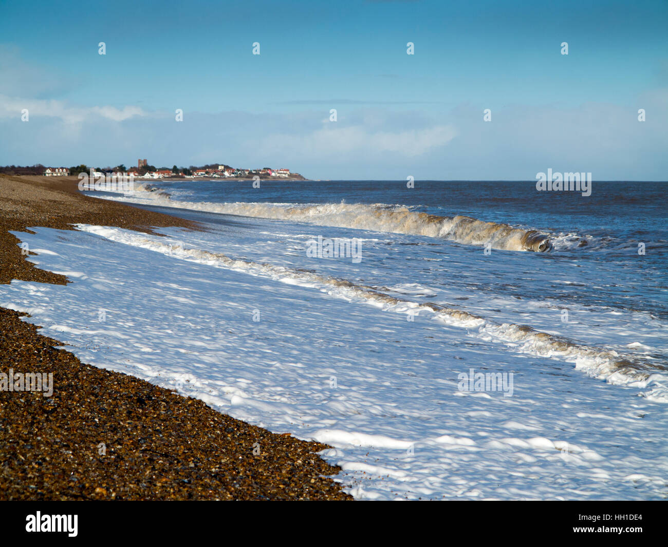 Waves breaking on the shoreline during heavy winds and spray with foam in the foreground with Thorpeness on the horizon Stock Photo