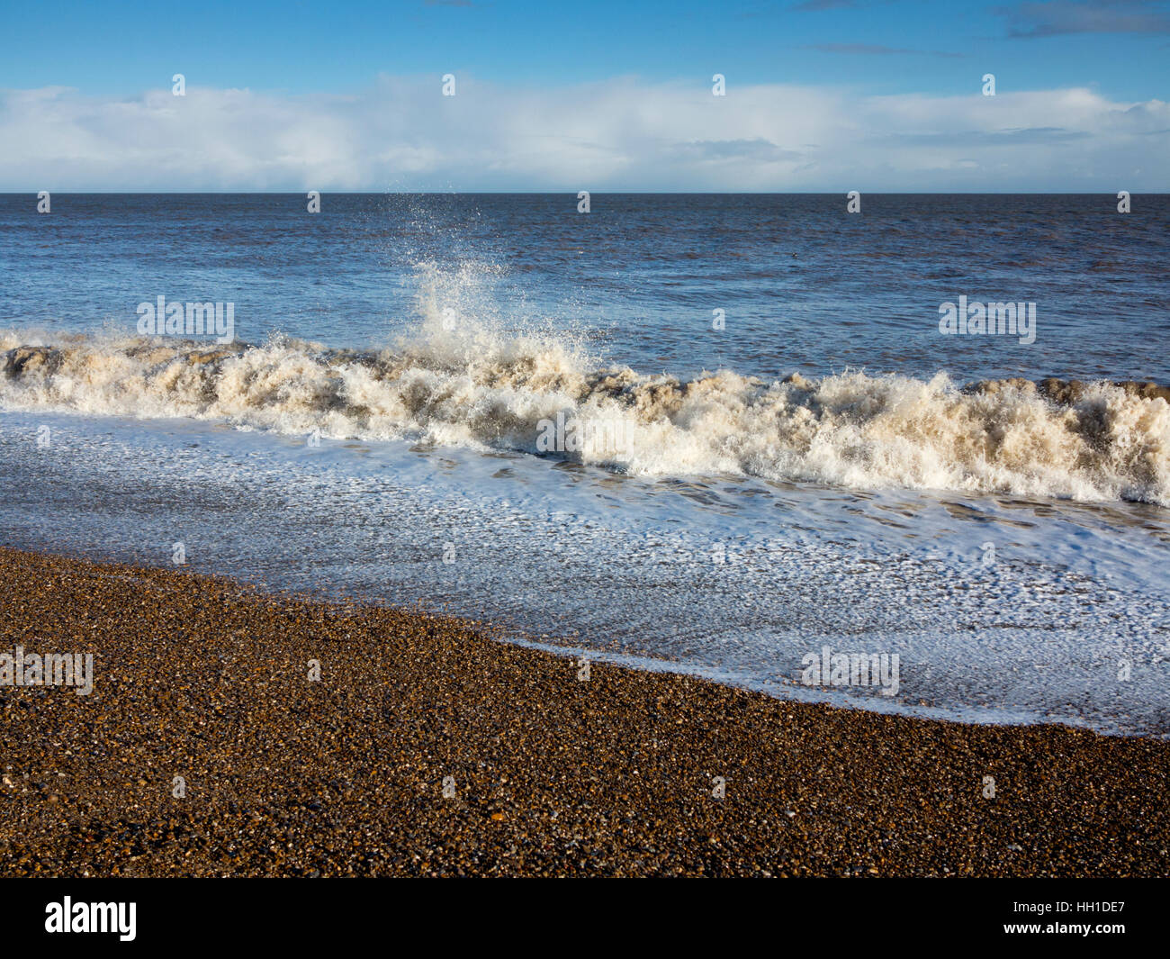 Churning waves breaking on the shoreline during heavy winds and spray with foam in the foreground, Aldeburgh, Suffolk Stock Photo