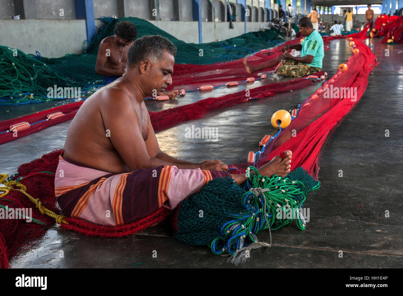 Local men repairing fishing nets in hall at harbour, Beruwela, Western Province, Sri Lanka Stock Photo