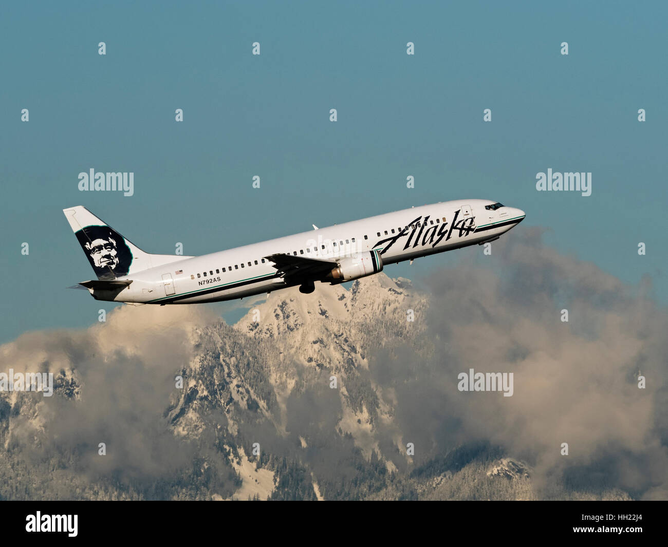 Alaska Airlines plane airplane Boeing 737 (737-400) N792AS narrow-body jetliner airborne snow-capped mountain backdrop Stock Photo