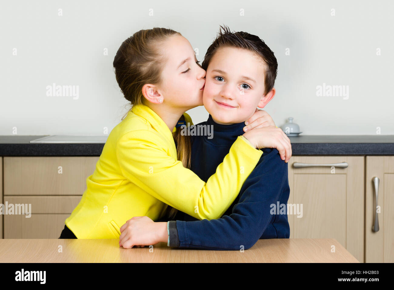 Young girl gives her brother a kiss at home in the kitchen Stock Photo