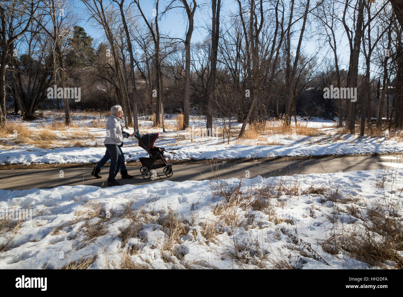 Wheat Ridge, Colorado - Two women walk with a toddler in a stroller on the Clear Creek Trail in winter. Stock Photo