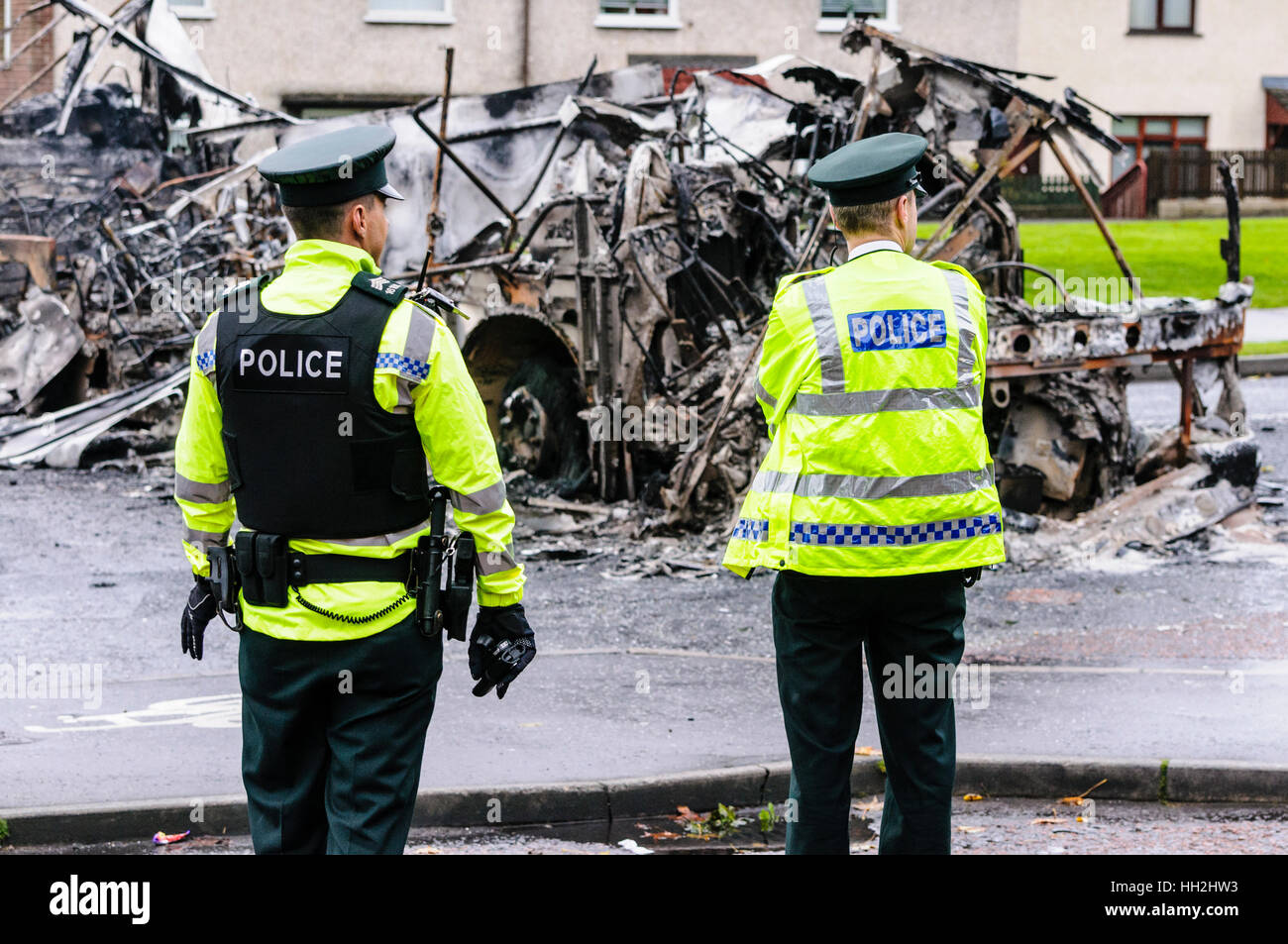 Two police officers at the scene of civil unrest, where a bus was hijacked and burned out. Stock Photo