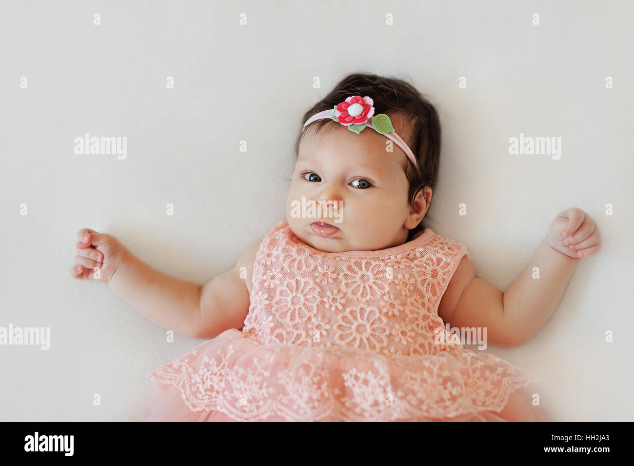 Small very cute wide-eyed smiling baby girl in a pink dress lying ...