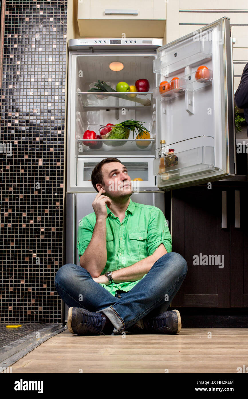 Young Man Sitting on the floor In Front Of Fridge with fruits and