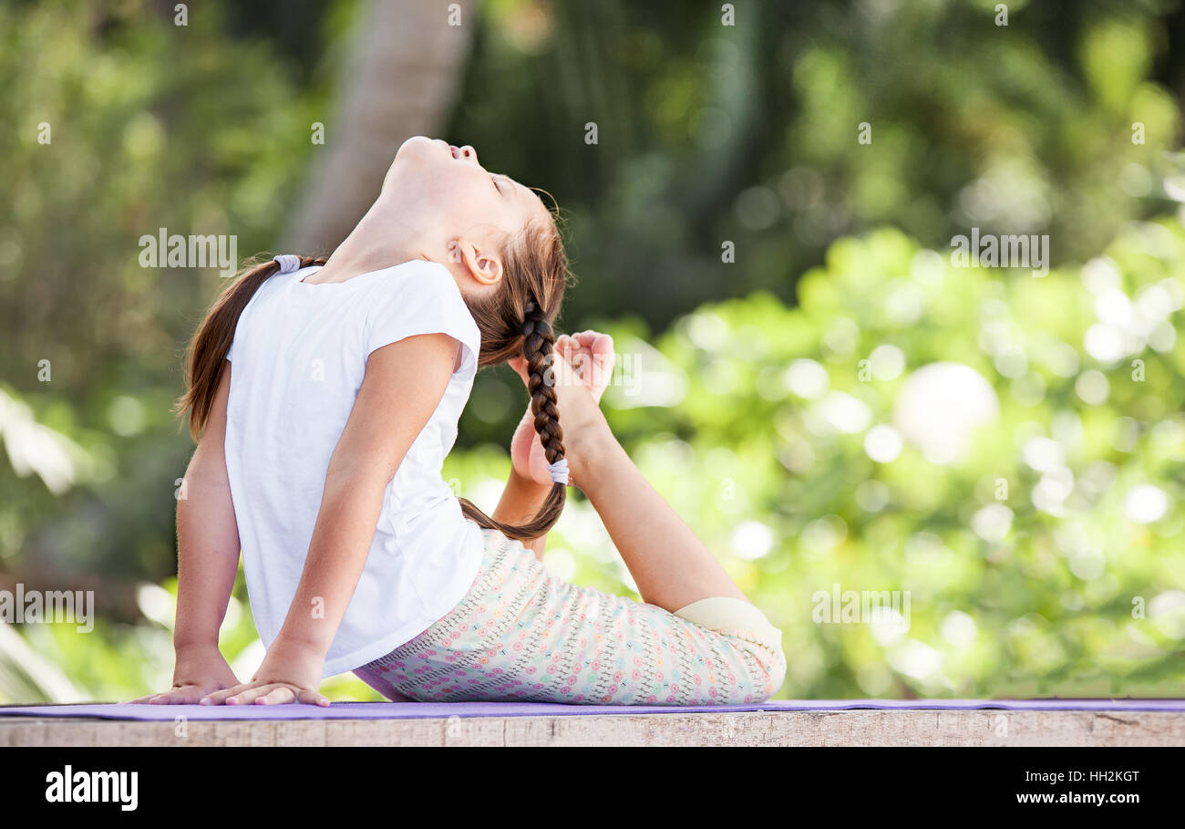 Child doing exercise on wooden platform outdoors. Healthy lifestyle. Yoga girl Stock Photo