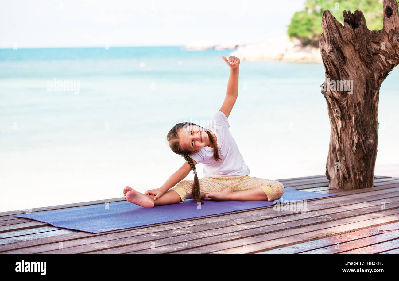 Child doing meditating exercise on wooden platform sea shore outdoors. Healthy lifestyle. Yoga girl Stock Photo