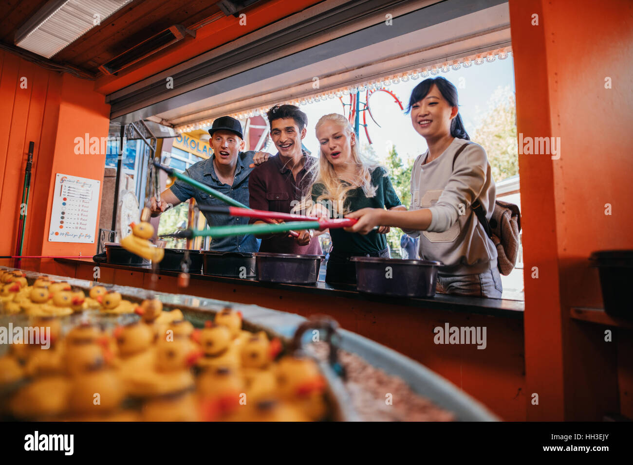 Happy young people having fun at amusement park playing fishing game. Group of friends playing fishing game at fairground. Stock Photo