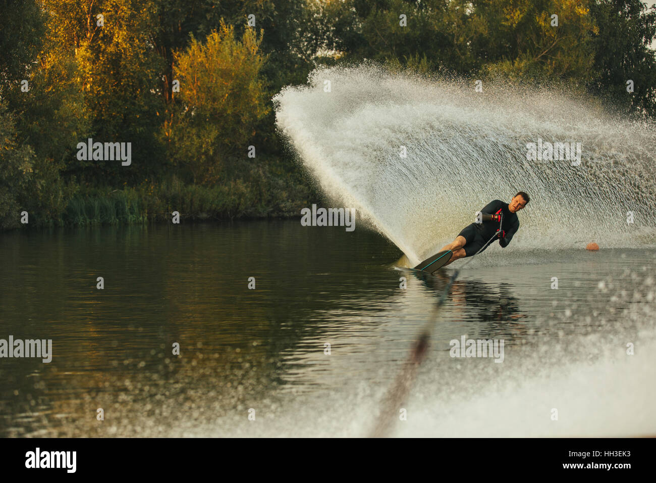 Wakeboarder skiing on lake with splash of water. Man practicing wakeboarding stunts. Stock Photo