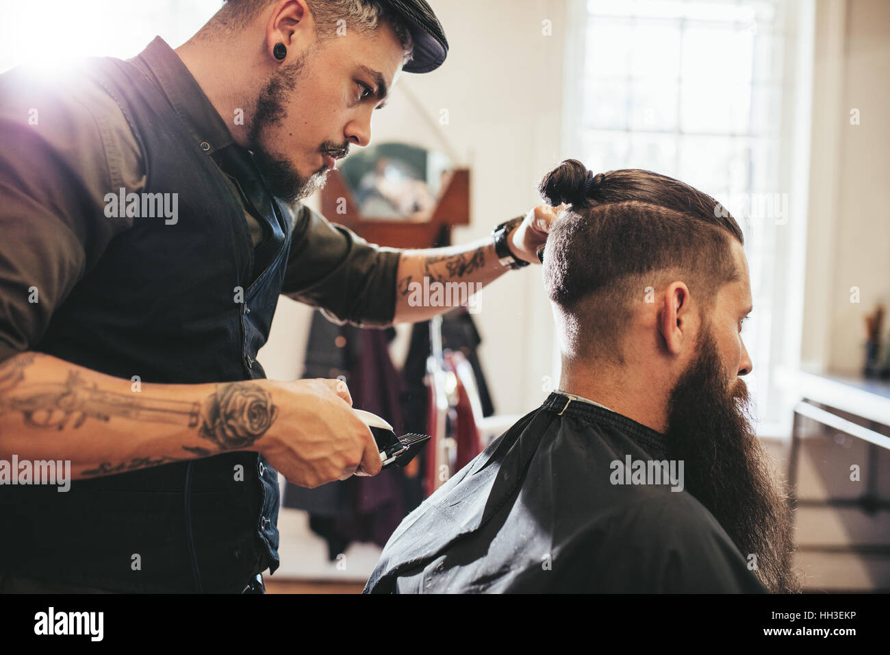 Stylish hairdresser cutting hair of client at barber shop. Beard man getting haircut at salon. Stock Photo