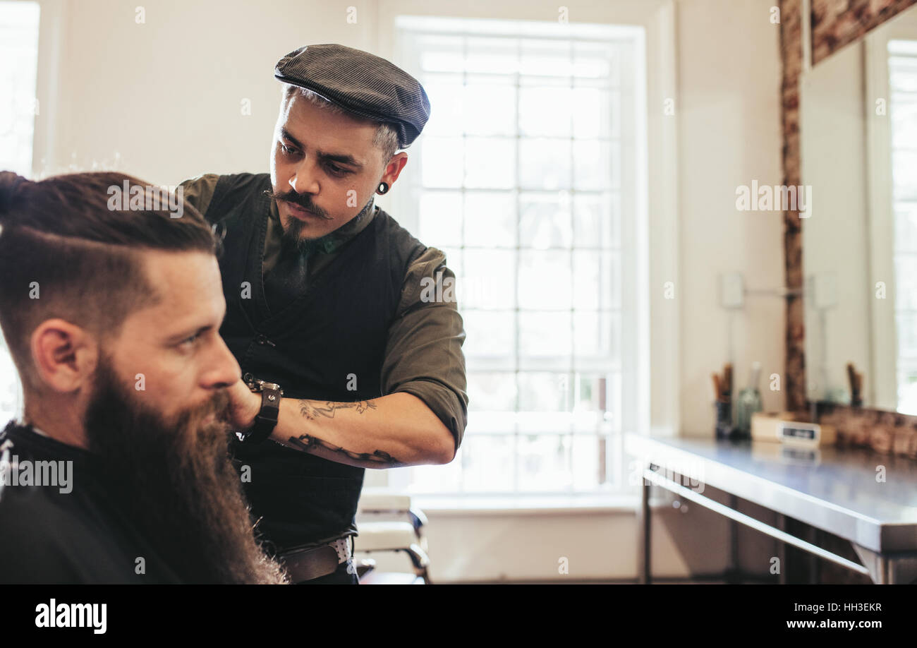 Stylish hairdresser cutting hair of client at salon. Beard man getting haircut at barber shop. Stock Photo
