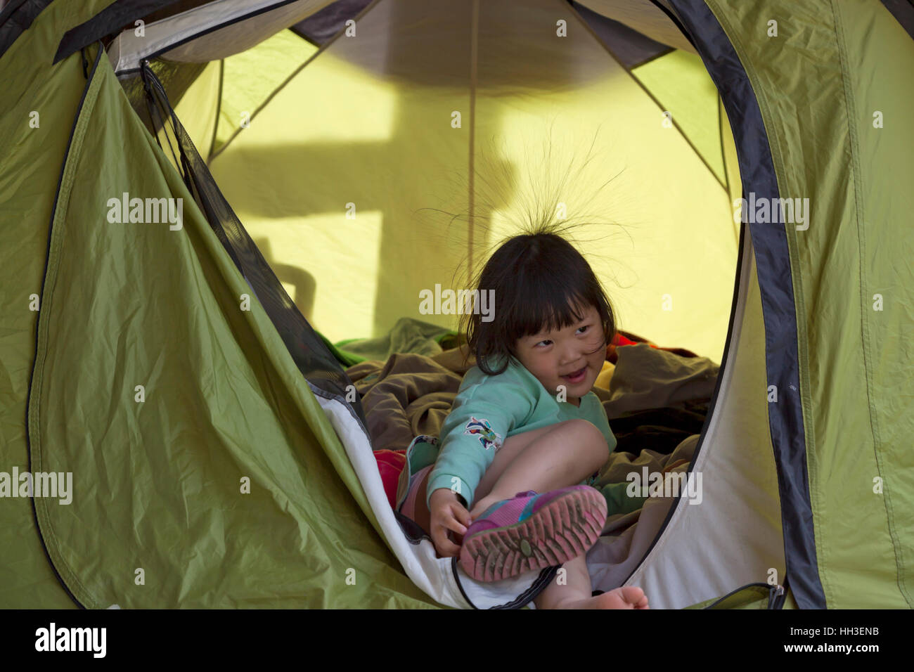 A Chinese little girl with some hair standing due to static electricity plays in a tent during a family camping trip in China. Stock Photo