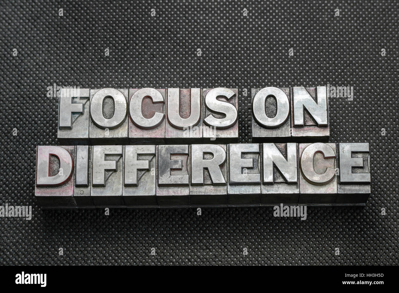 focus on difference phrase made from metallic letterpress blocks on black perforated surface Stock Photo