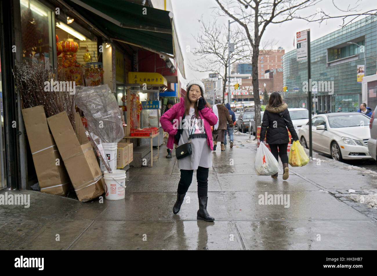 A pregnant woman talking on her cell phone on an overcast winter day. In Chinatown, downtown Flushing, Queens, New York City. Stock Photo