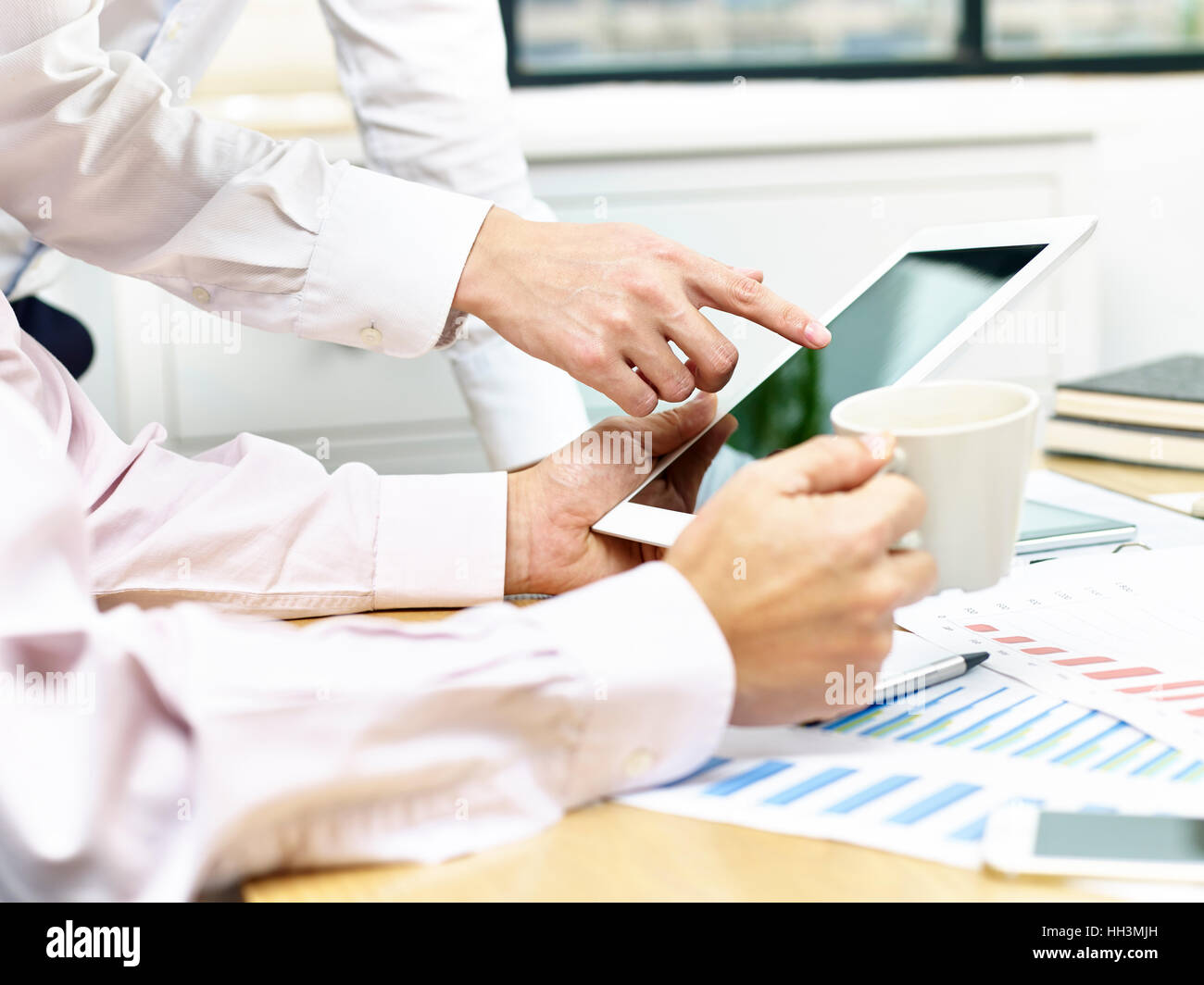 two business executives sitting at desk discussing sales performance using tablet computer. Stock Photo