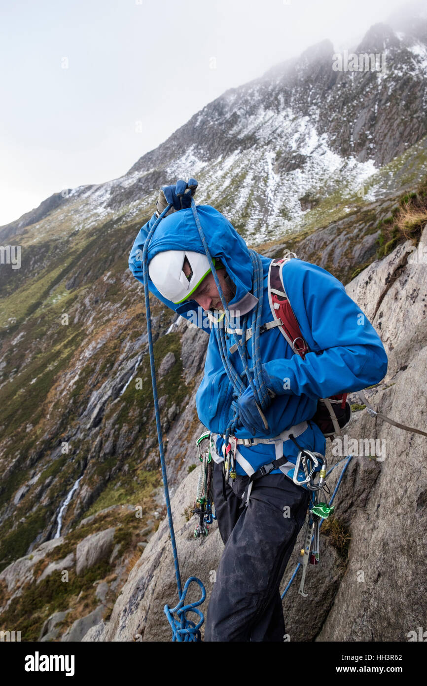 A mountain climber coiling a climbing rope around his body preparing to