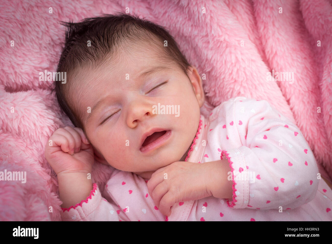 A less than three weeks of age cute baby girl, sleeping with mouth open on a pink blanket. Nouveau-né dormant bouche ouverte. Stock Photo