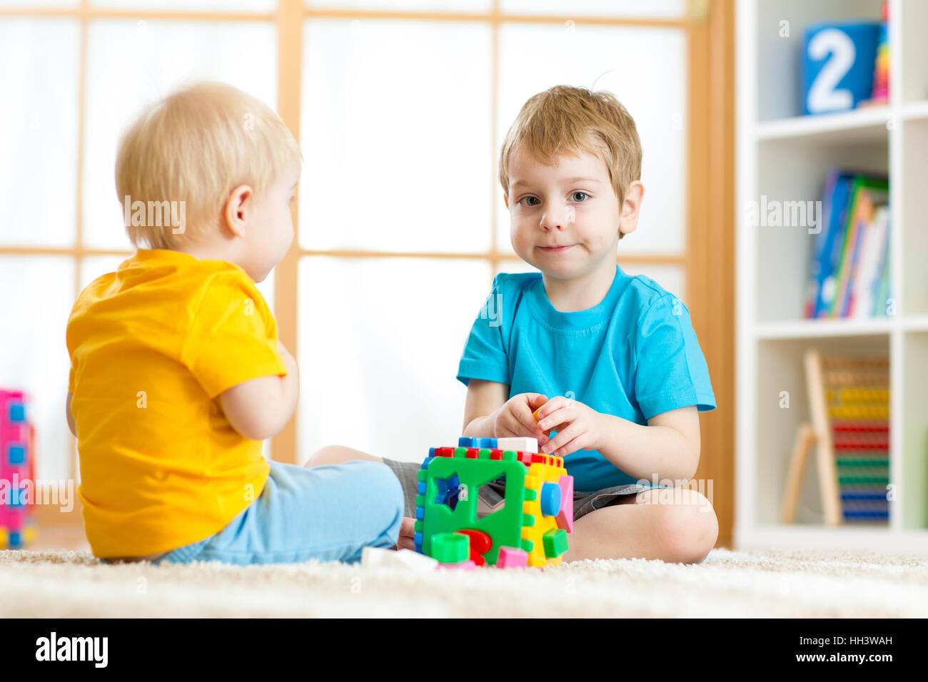 Children boys playing with logical educational toys, arranging and sorting shapes and sizes Stock Photo
