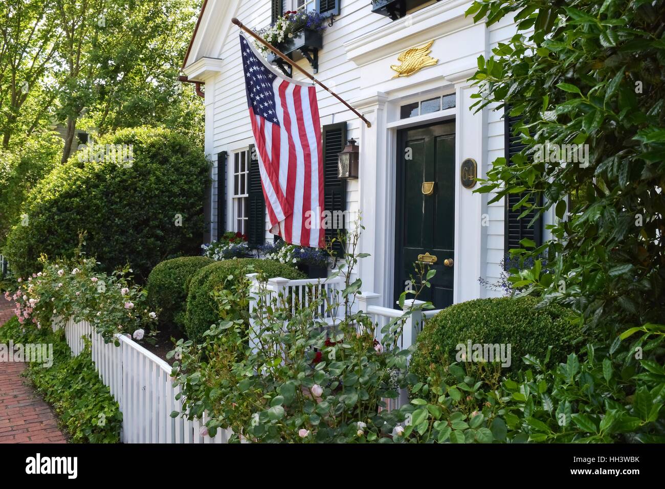 White New England old colonial home with a white picket fence and an American flag hanging outside on Martha's Vineyard, MA USA Stock Photo