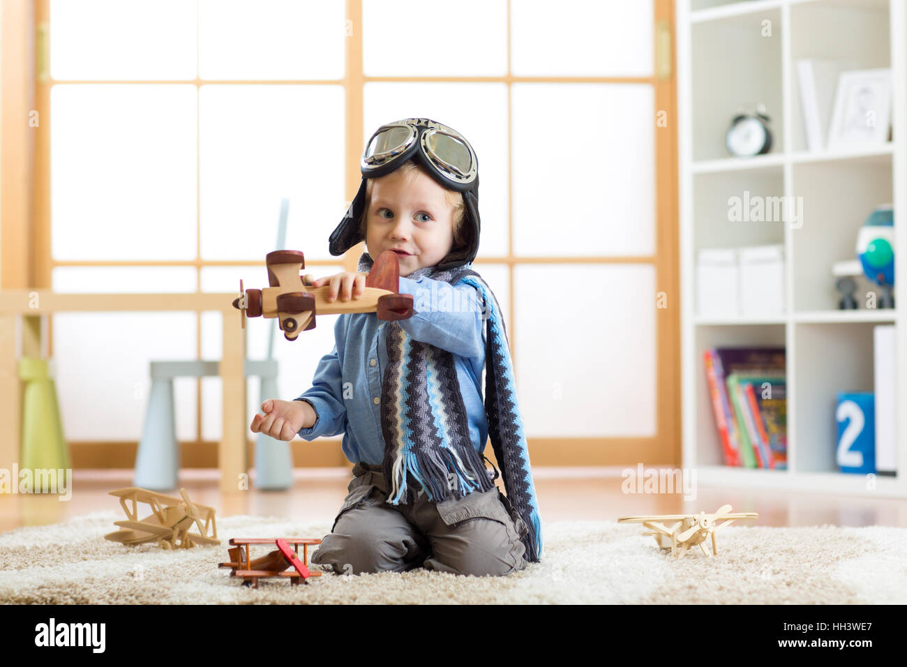 Child dressed like pilot aviator plays with a toy airplanes at home on floor in his room Stock Photo