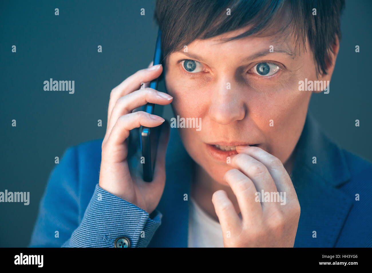 Nervous businesswoman bites fingernails during telephone conversation on mobile phone Stock Photo
