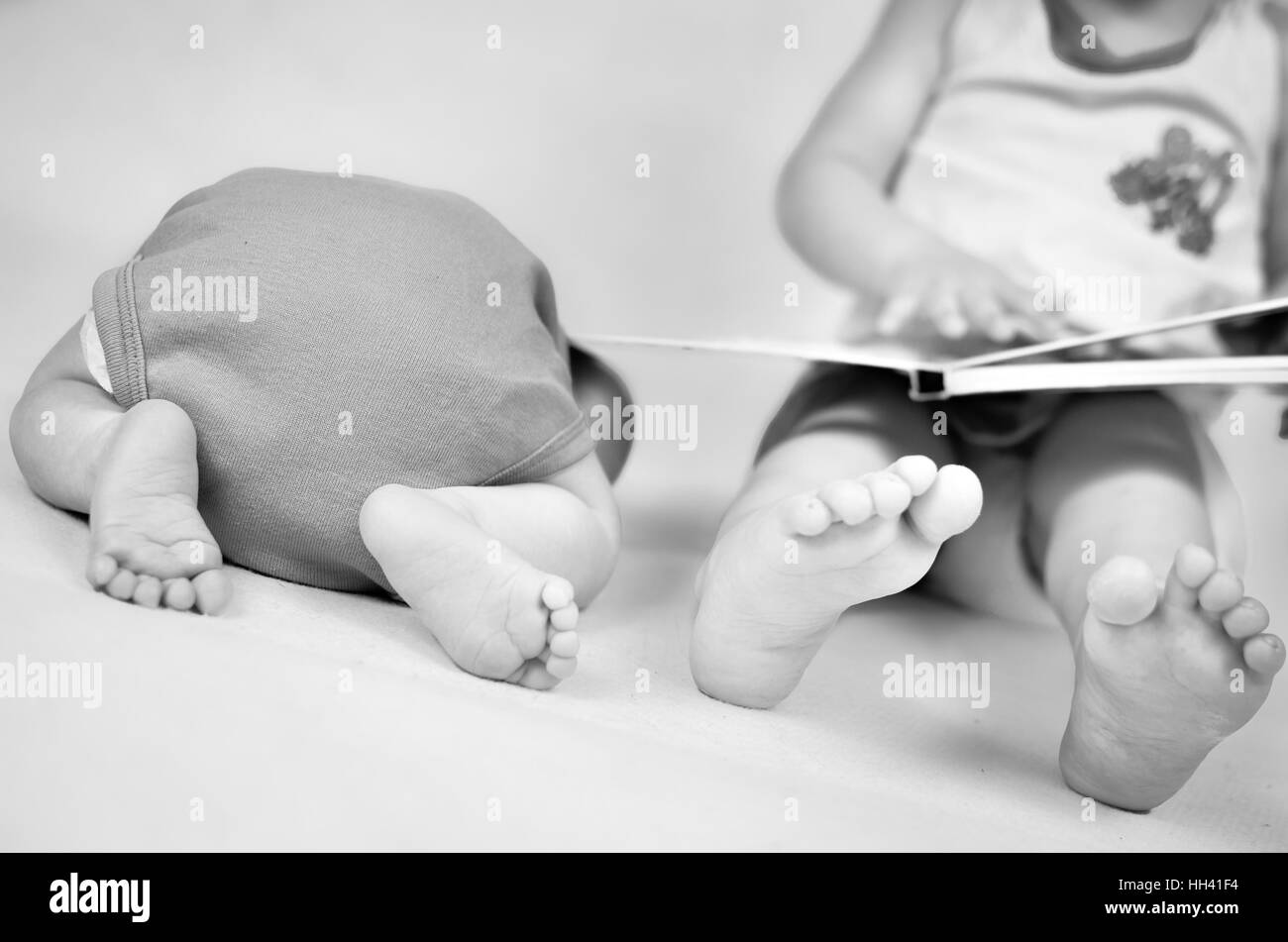 Little girl is reading a book tog her baby brother. Black and white photo with soft focus on their feet. Family values Stock Photo