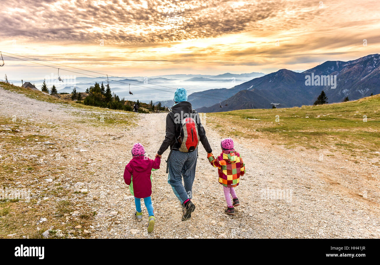 Family hiking in the mountains on ski slope into sunset. Mother and two ...