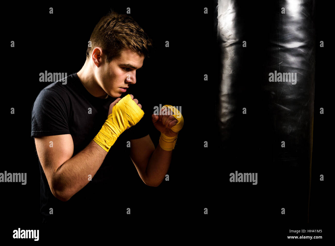 Attractive young man in yellow boxing wraps is training and hitting heavy bag. Fitness, aerobic exercise for active people. Strong athlete isolated on Stock Photo
