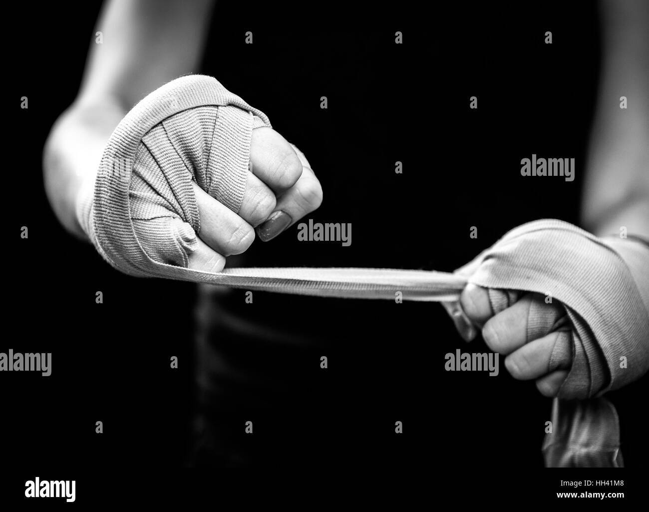 Woman is wrapping hands with pink boxing wraps. Isolated on black with red nails. Strong hand and fist, ready for fight and active exercise Stock Photo