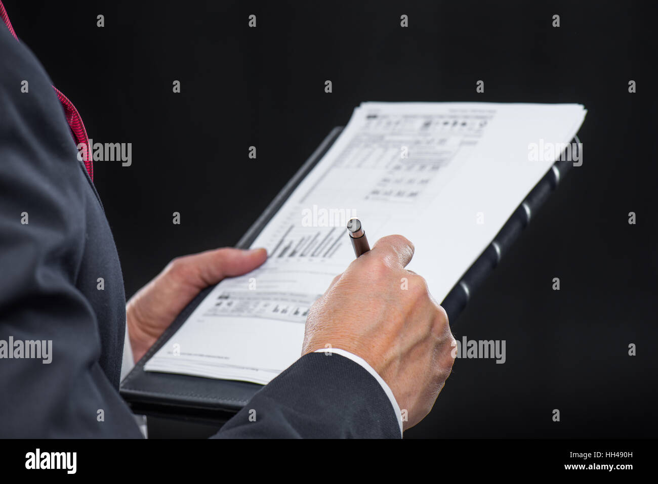 Close-up partial view of businessman holding papers and writing with pen Stock Photo
