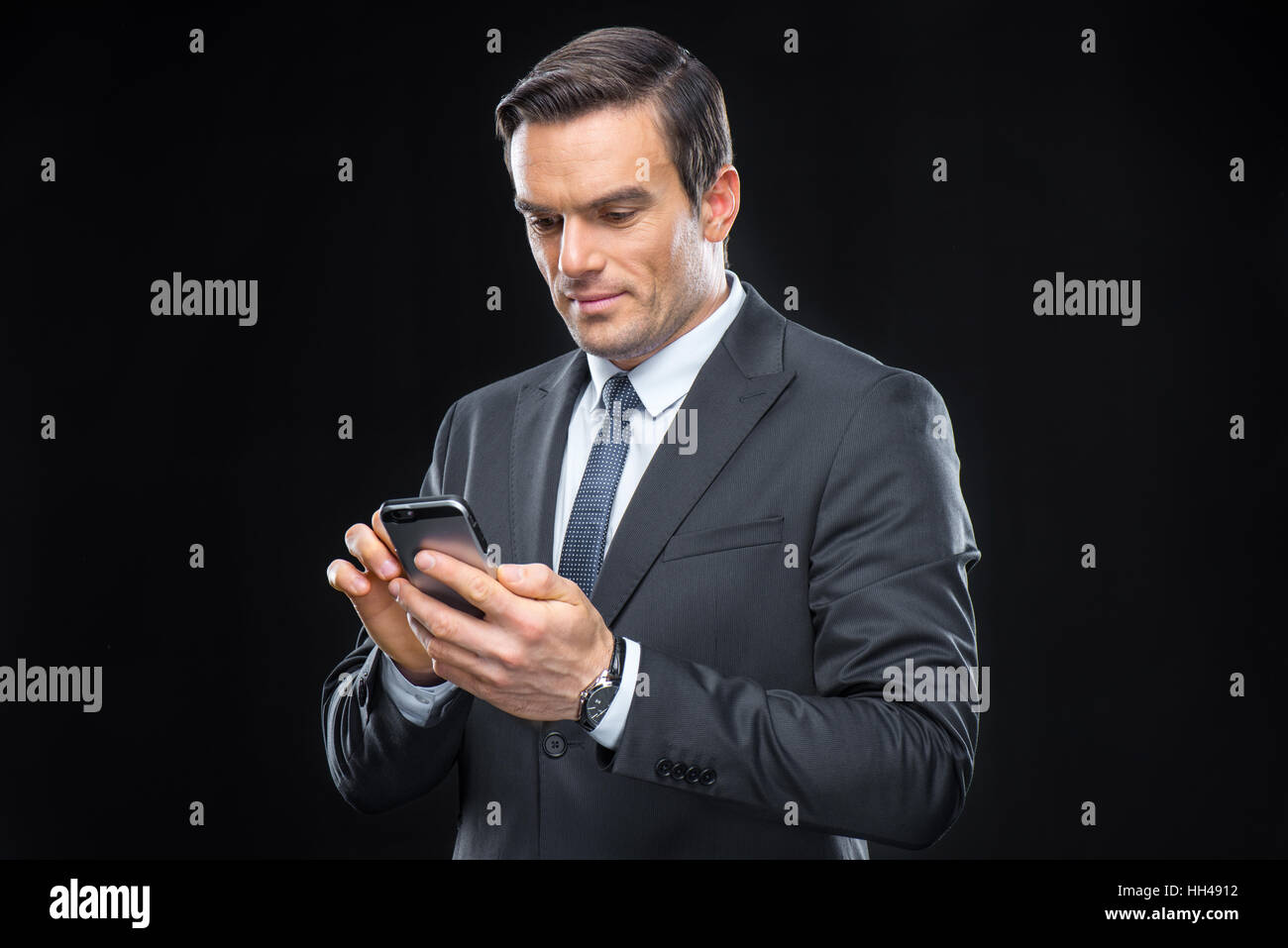 Smiling handsome businessman using smartphone on black Stock Photo