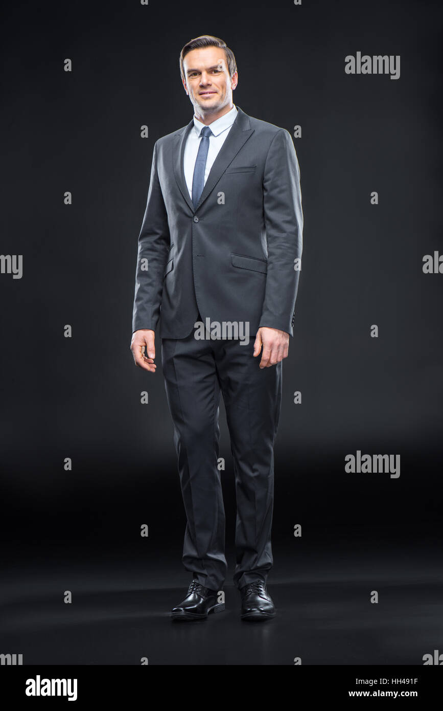 Full length portrait of handsome businessman in suit posing on black Stock Photo