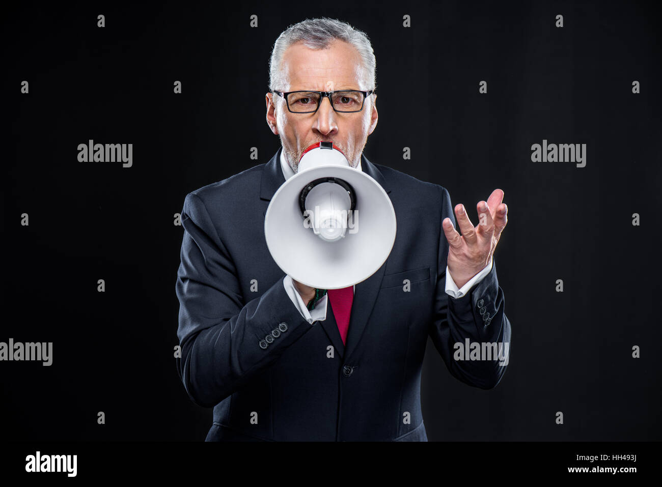 Mature businessman in eyeglasses speaking with loudspeaker on black Stock Photo