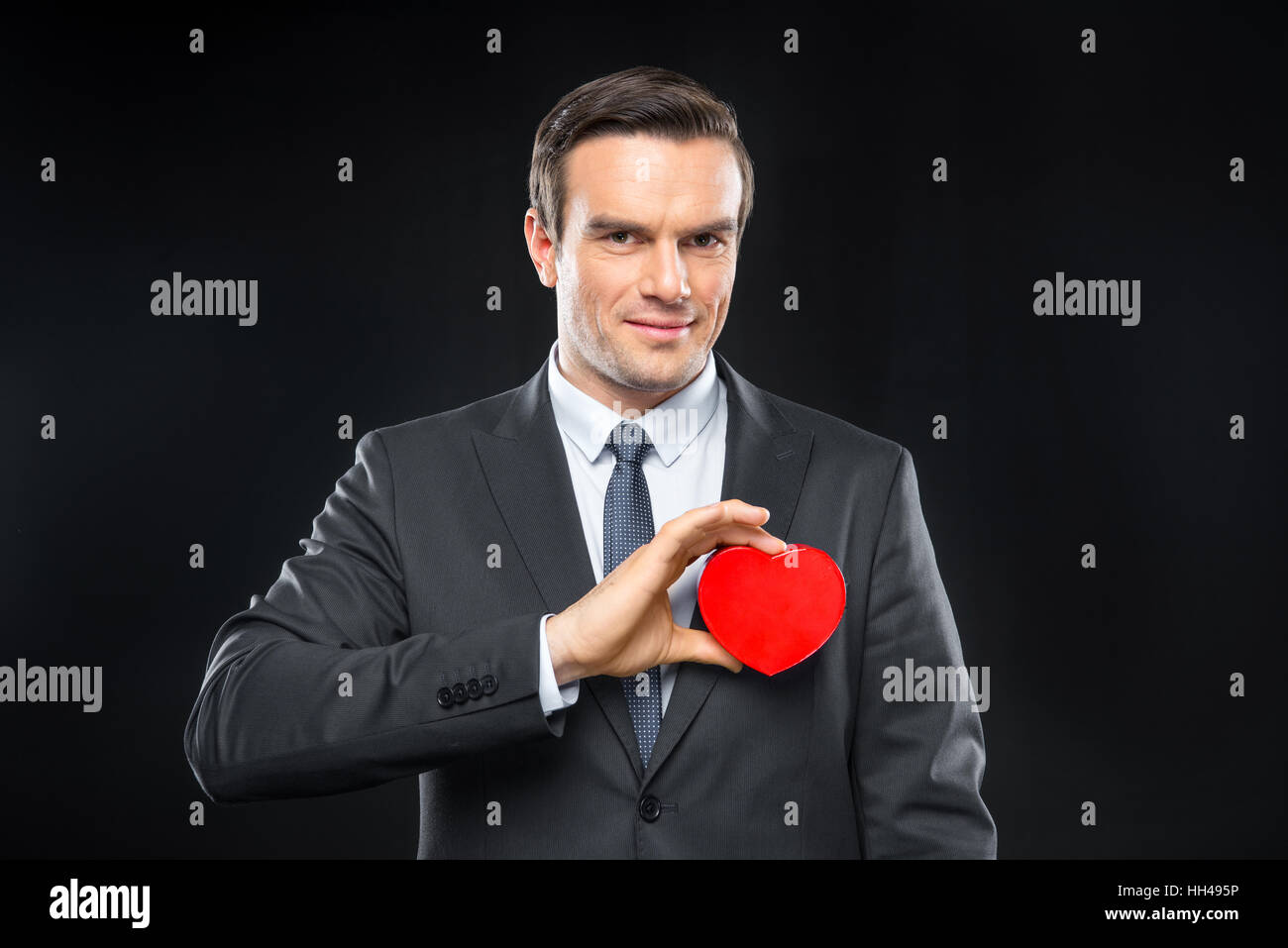Handsome man hoding red toy heart smiling and looking at camera on white Stock Photo