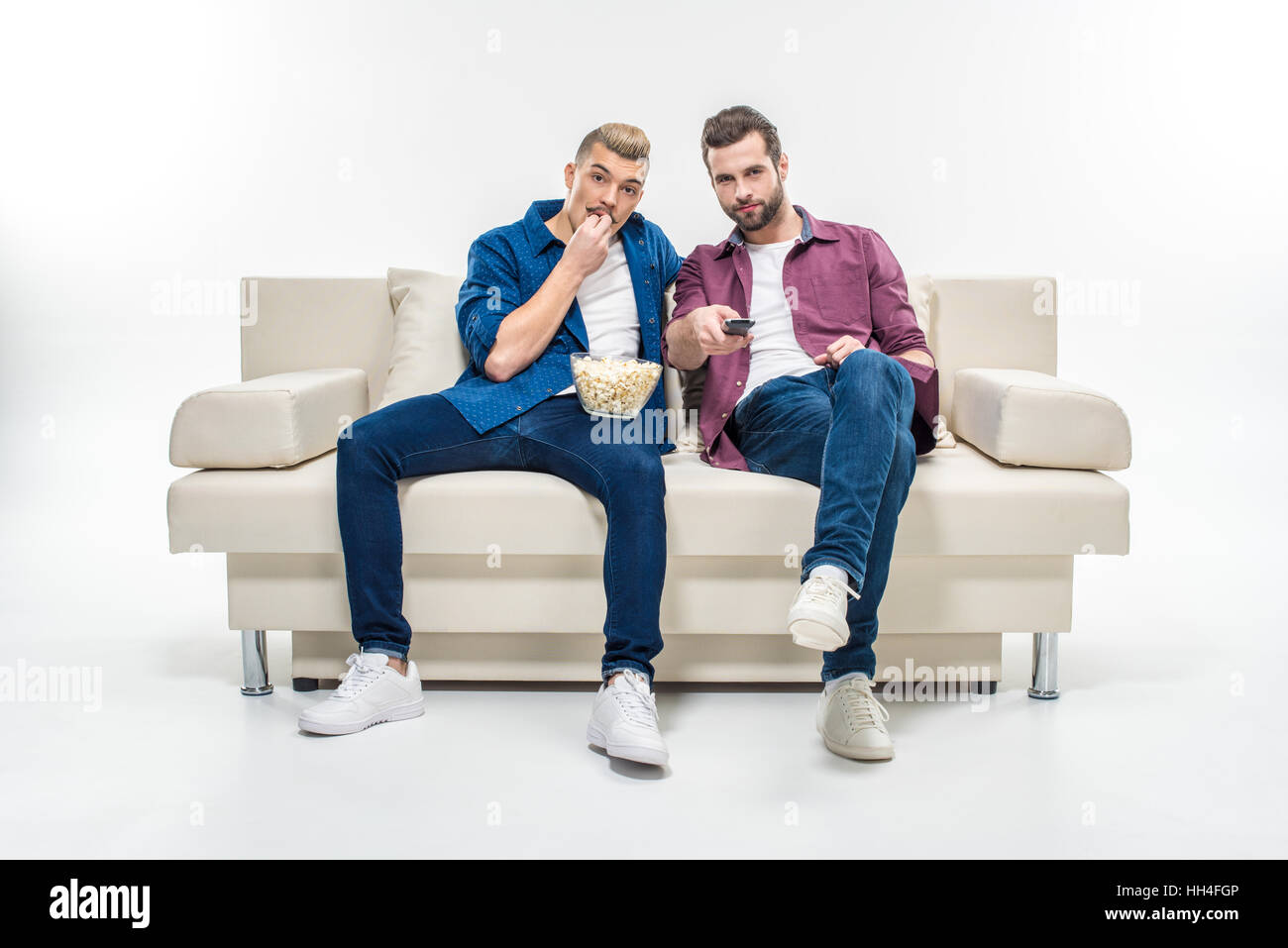 Male Friends Sitting On Couch With Popcorn And Watching Tv Stock