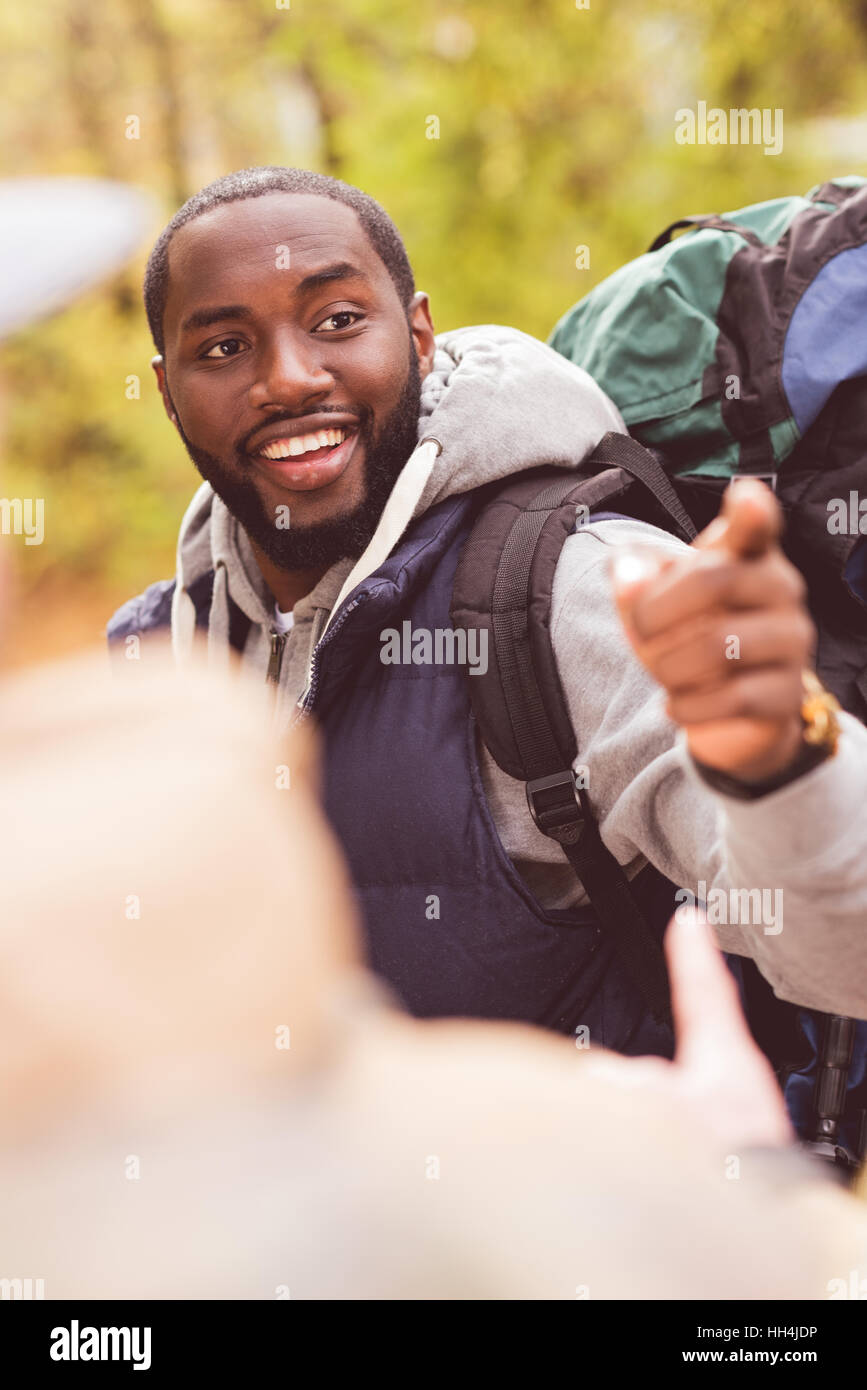 Young smiling man backpacker pointing with finger and talking with blurred male friend on foreground Stock Photo