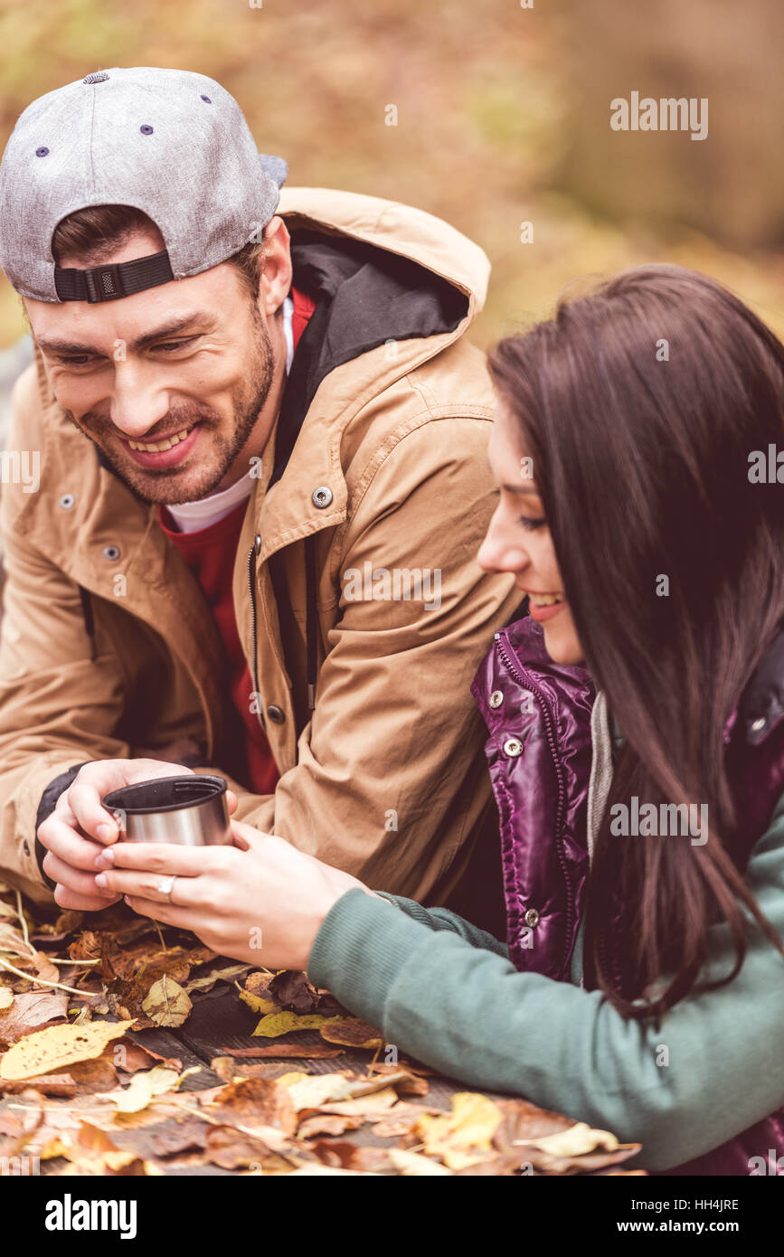 Close-up view of young smiling man giving cup from thermos with hot drink to beautiful brunette woman Stock Photo