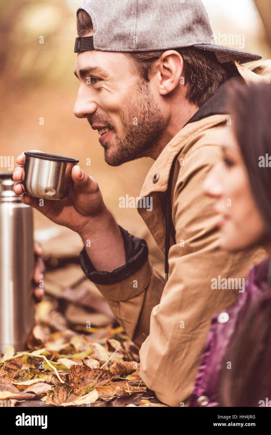 Side view of handsome young man sitting near brunette woman and holding cup from thermos with hot drink Stock Photo