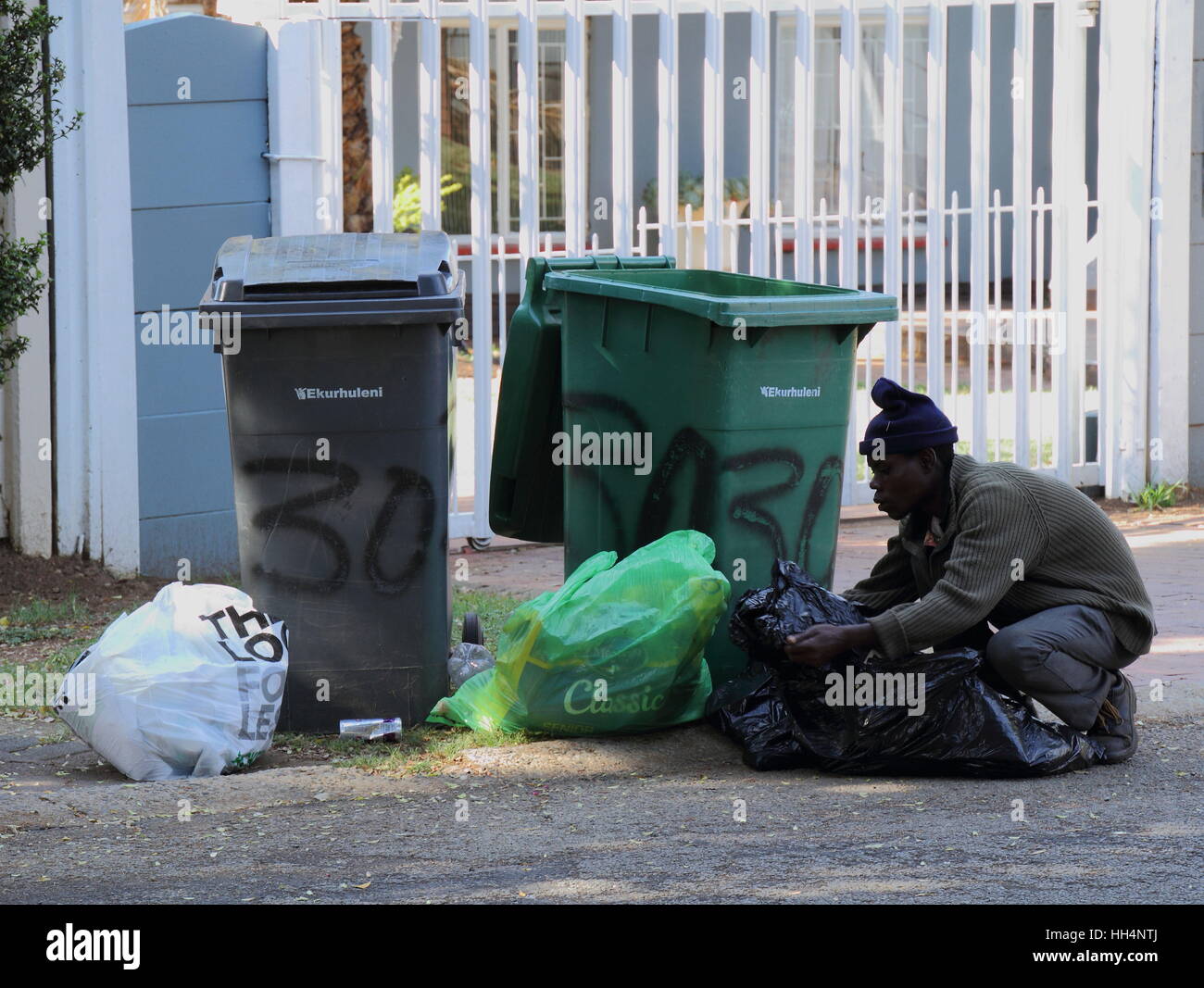 Homeless man digs through residential refuse bins for food and reusable