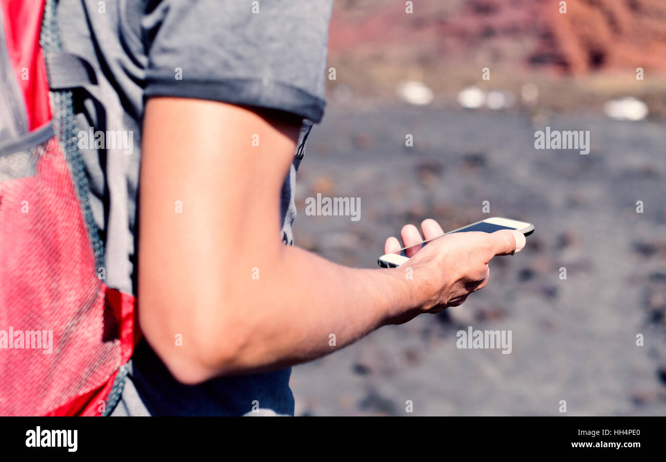 closeup of a young caucasian man carrying a backpack using a smartphone outdoors, in the mountain Stock Photo
