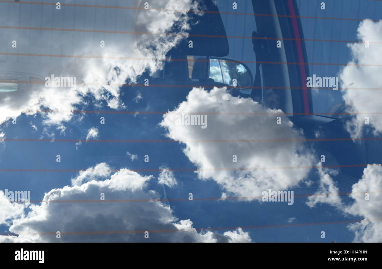 clouds and blue sky reflected in car rear windscreen, interior of car and mirror just visible Stock Photo