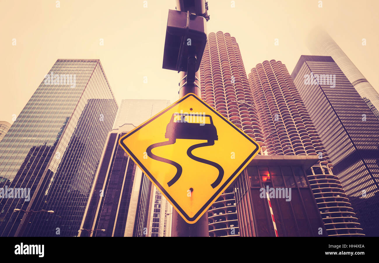 Color toned slippery when wet road sign with curvy tracks, Chicago skyscrapers in distance, conceptual picture. Stock Photo