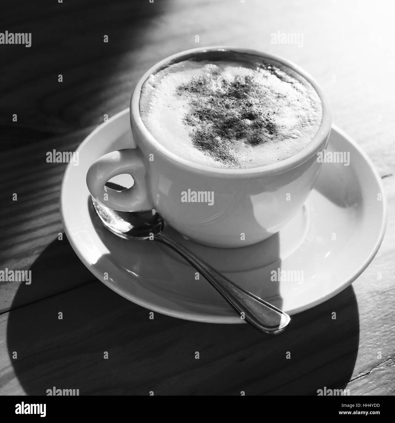 Cappuccino. Cup of coffee with milk foam and cinnamon powder stands on wooden table, square black and white photo Stock Photo
