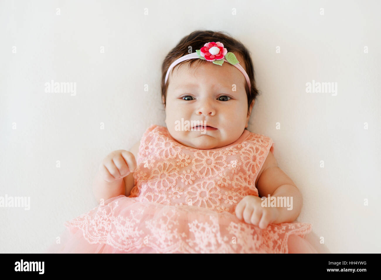 cute baby girl with sad face lies on a white blanket Stock Photo